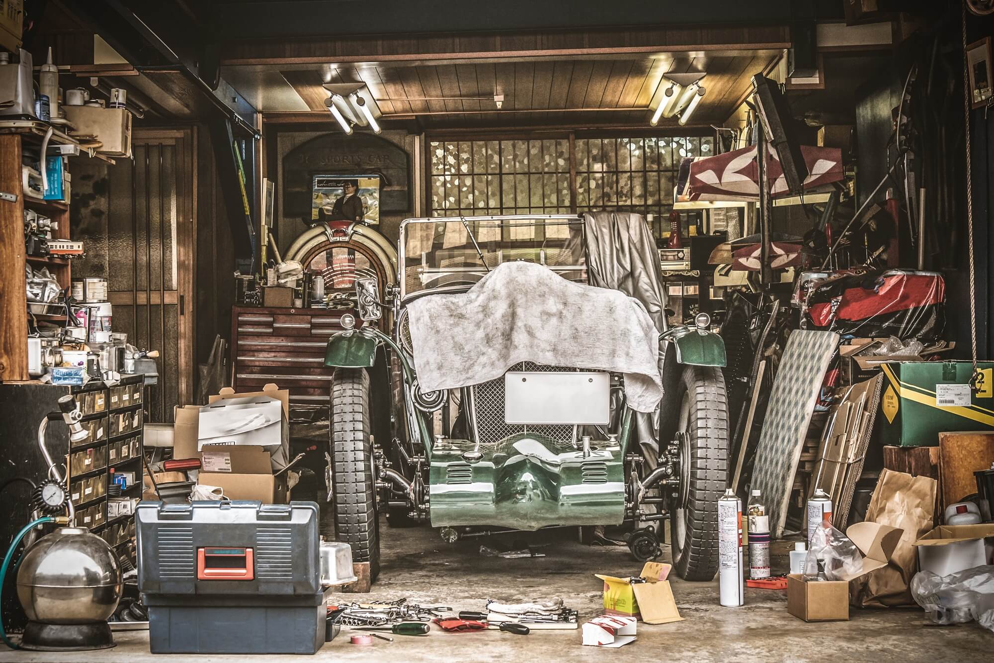 Retro vintage car covered by white cloth. Renovation project in the garage with lots of mechanical details and tools